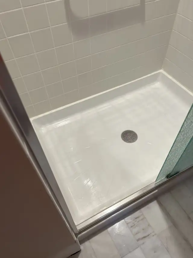Refinished bright white shower floor and white tile walls behind a glass door