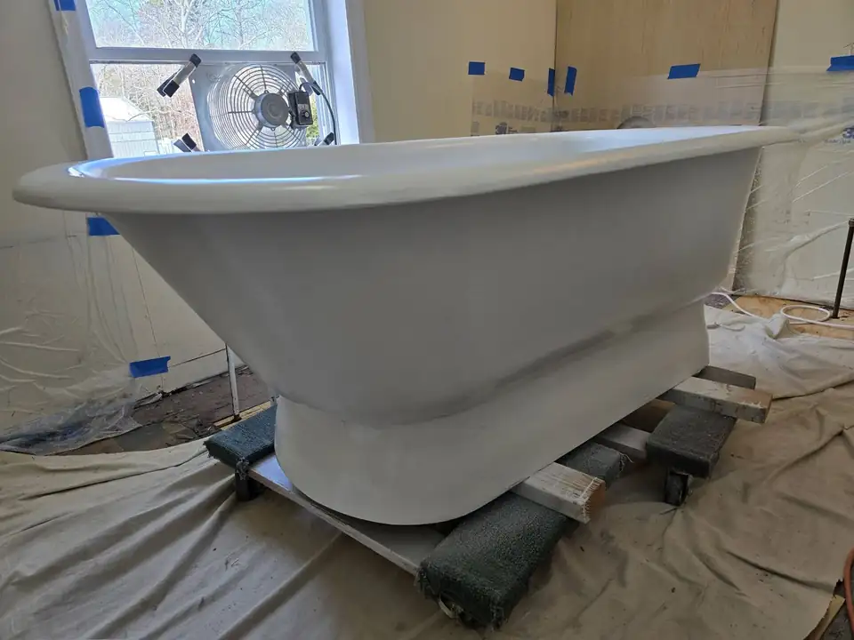 Cast iron pedestal bathtub freshly reglazed glossy white in a masked-off room, tub reglazing in Toms River, NJ