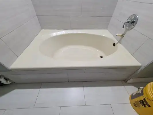 Oval drop-in soaking tub refinished in a bone finish, surrounded by gray wall and floor tile